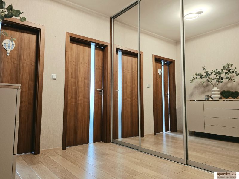 A hallway with a mirrored wardrobe, a floor with a wood decor, and doors in a 4-room apartment.
