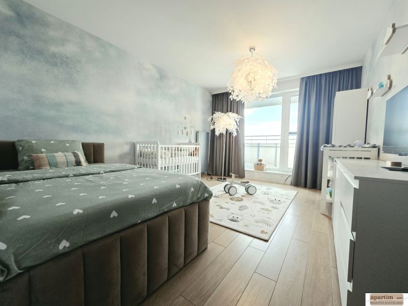 Bedroom in a 4-room apartment with wood-patterned flooring, a bed, and a baby crib.