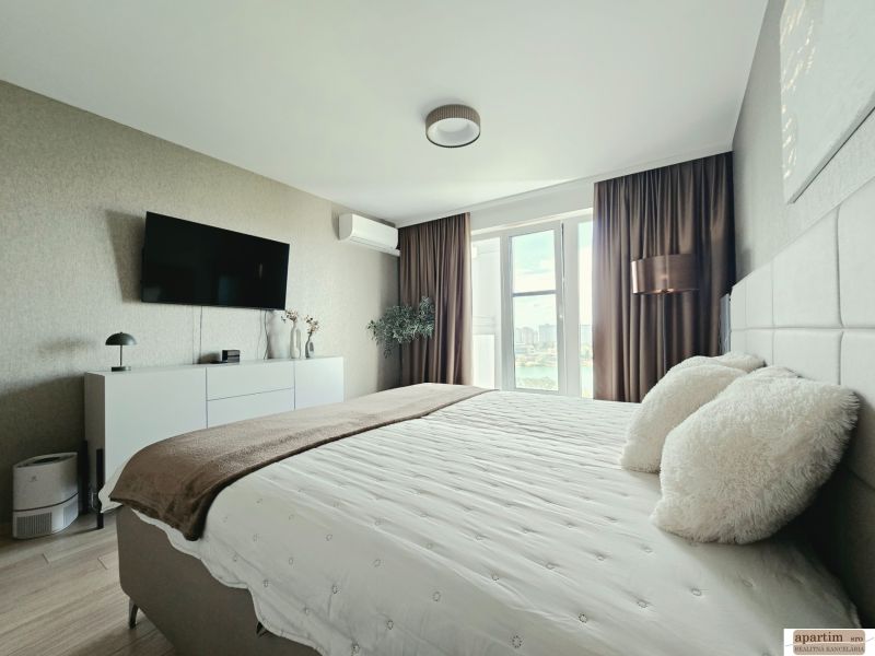 A stylish bedroom in a 4-room apartment with a wooden decor floor and a view through a large window.