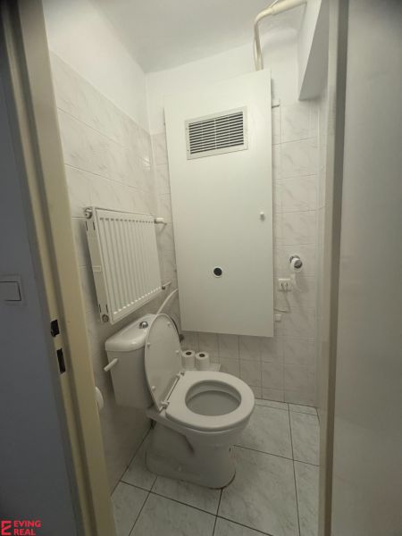 Bathroom in a studio apartment with a toilet, light tiles, and a radiator.