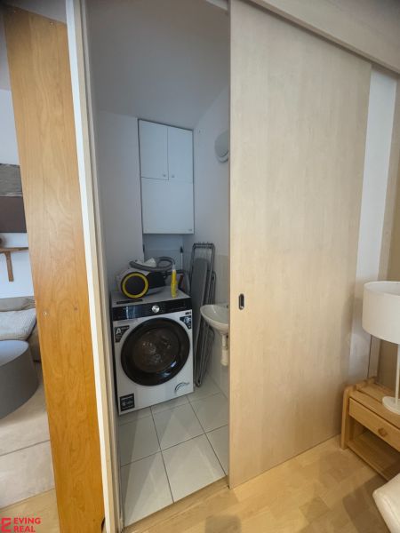 A bathroom in a studio apartment with a washing machine and sliding doors, flooring with a wooden decor.