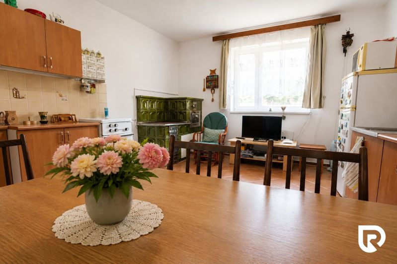 A kitchen in a family house with a tiled stove, a dining table, and floral decoration.