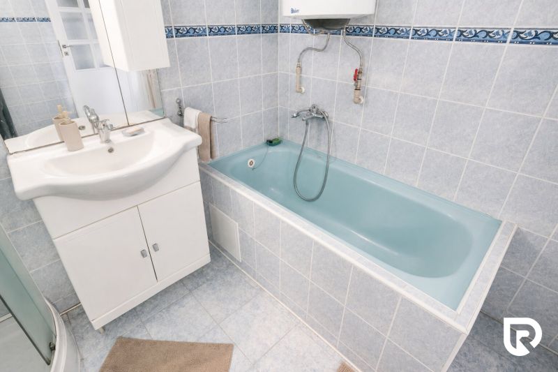 A bathroom with a white sink cabinet and a blue bathtub in a family house.