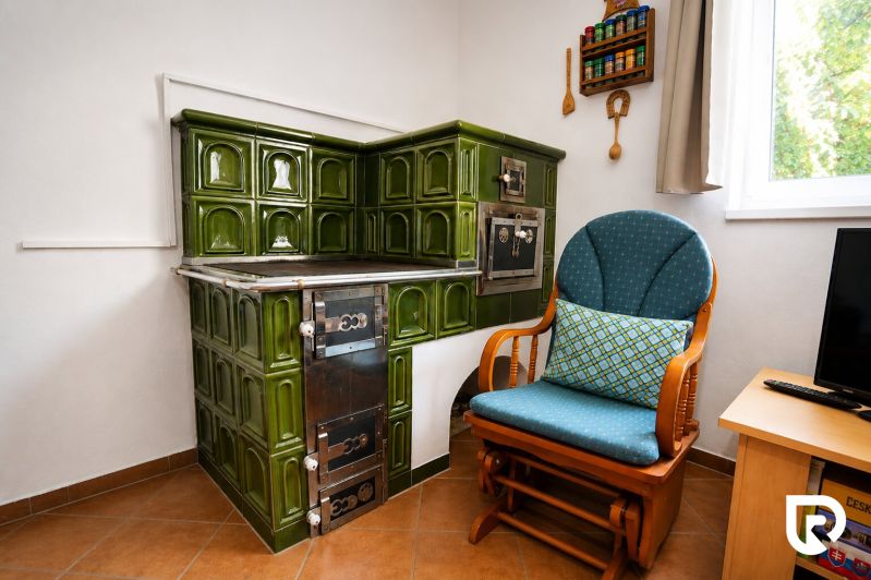 A tiled stove with green tiles next to an armchair in a family house.