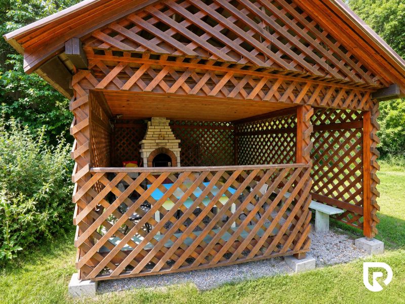 A gazebo with a wooden lattice and an outdoor grill in the garden by the family house.