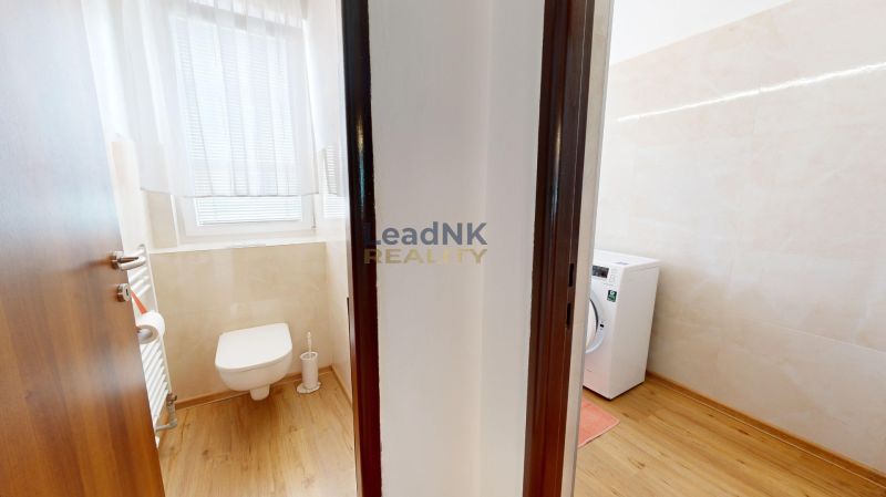 A bathroom in a 3-room apartment with a toilet, washing machine, and a floor with a wooden decor.