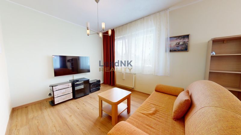 Living room in a 3-room apartment with a wooden decor floor, a sofa, and a television.