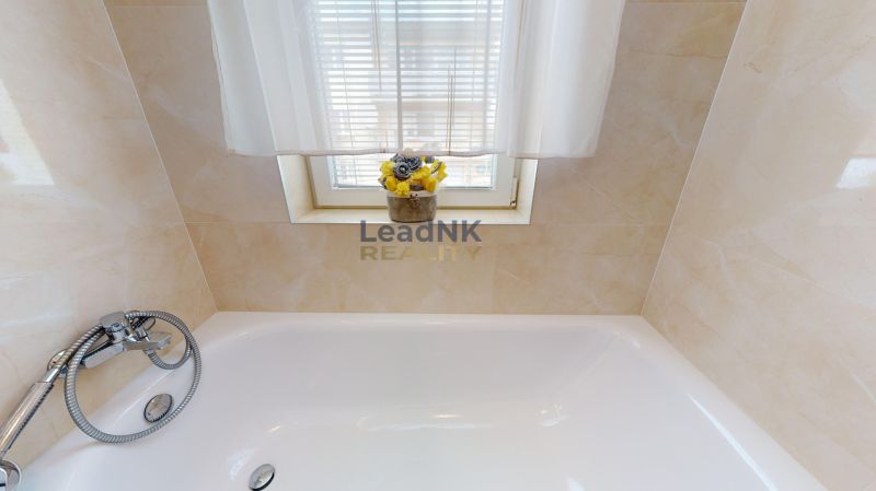 A bathroom with a shower faucet, a bathtub, and flowers on the windowsill in a three-room apartment.