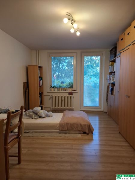 A room in a 3-room apartment with a bed, shelves, and a floor with a wood decor.