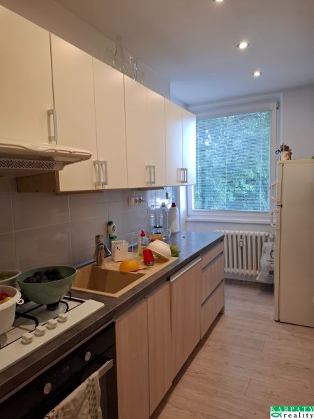 A kitchen in a 3-room apartment with a wooden decor floor and light cabinets.