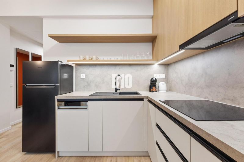 A kitchen in a studio apartment with a wood-patterned floor and a black refrigerator.