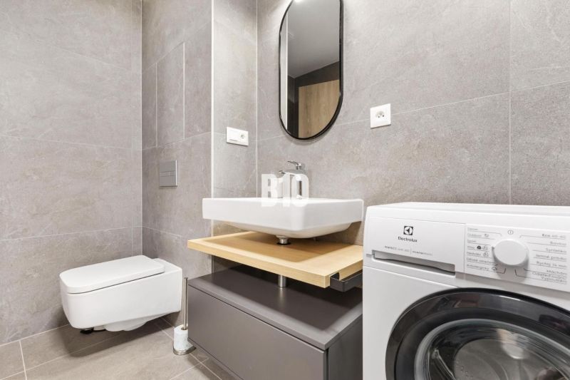 Bathroom in a studio apartment with a modern washing machine and gray tiles.