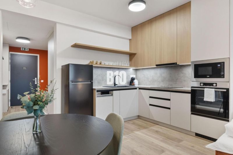 A kitchen with a dining table, appliances, and a wooden decor floor in a studio apartment.