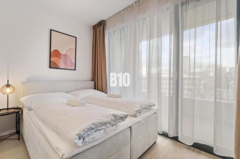 A bedroom with a bed, a nightstand, a painting, and sheer curtains in a studio apartment.