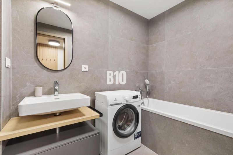 A bathroom with a sink, washing machine, and bathtub in a studio apartment.