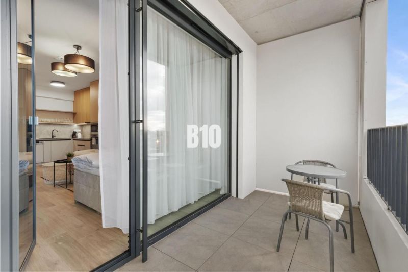 A balcony with seating and a view into a studio apartment through sliding doors.