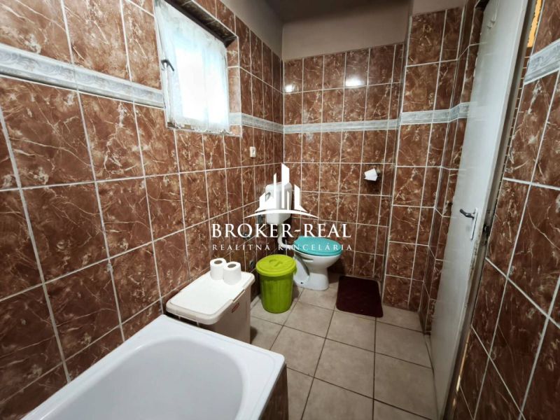 A bathroom with brown tiles, a bathtub, a toilet, and a waste bin in a family house.