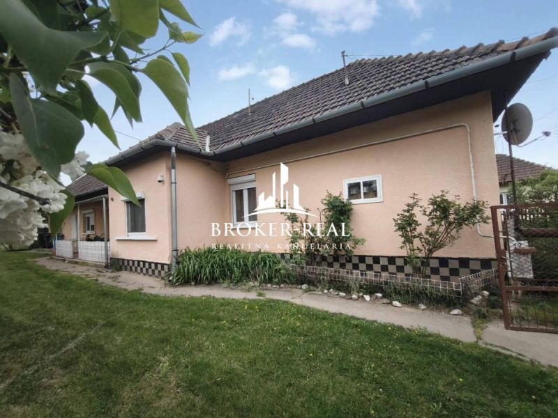 A family house in Bódvaszilas with light-colored walls, a sloping roof, and a green lawn.