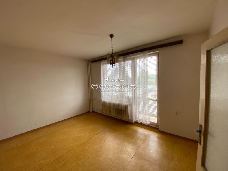 An empty room in a family house with a window, curtains, and a wooden-patterned floor.