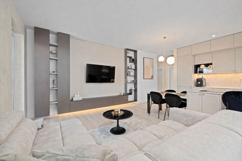 A bright living space in a 3-room apartment with a wooden decor floor and a kitchen unit.