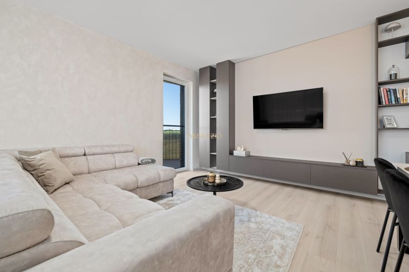 Living room with a beige sofa, a wall-mounted television, and a wood-patterned floor.