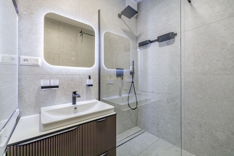 A bathroom in a 3-room apartment with a shower, mirror, and sink.