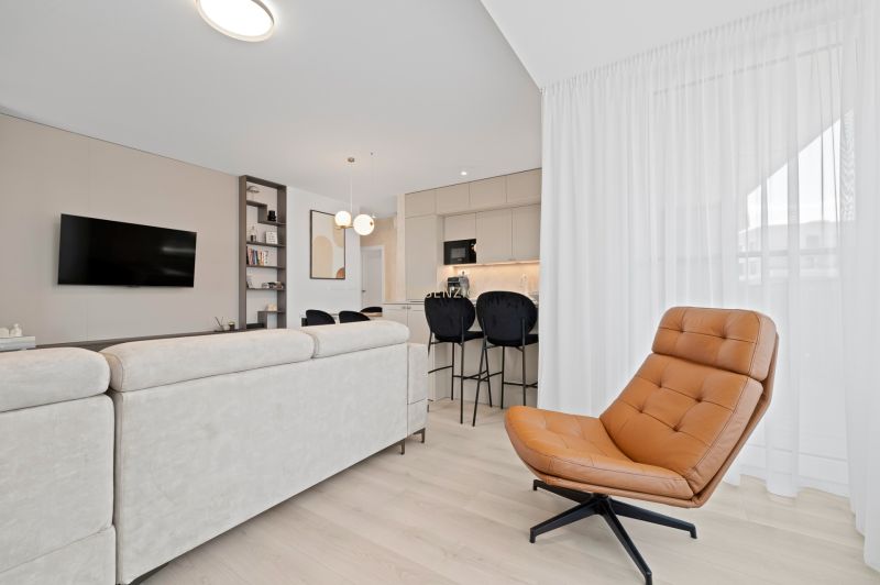 Living room in a three-room apartment with a wooden decor floor, a cream sofa, and a leather armchair.