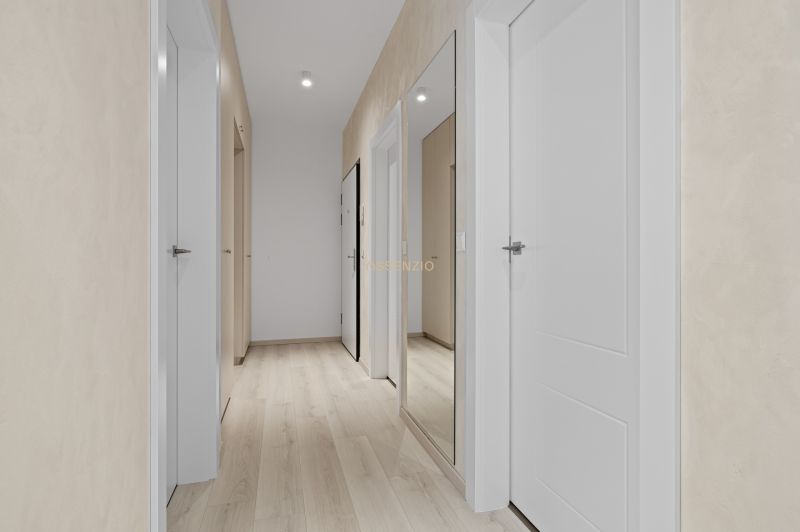 A hallway with white doors, a mirror, and a wooden decor floor in a 3-room apartment.