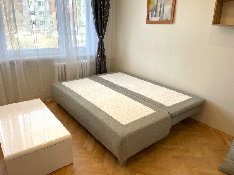 Studio apartment with a bed, wood-patterned floor, and a white table.