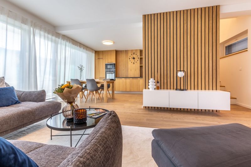 Living room in a family house with wood-patterned flooring and a dining area in the background.