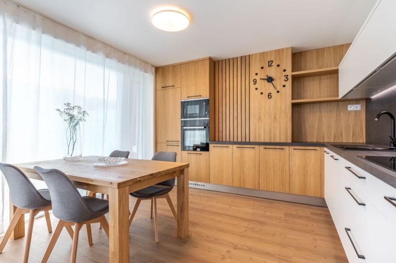 A kitchen with wooden decor, a dining table, gray chairs, and large windows.