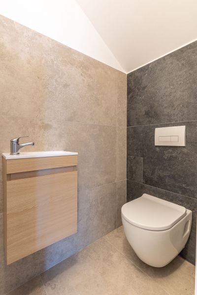 A bathroom in a family house with a toilet and a wooden cabinet under the sink.
