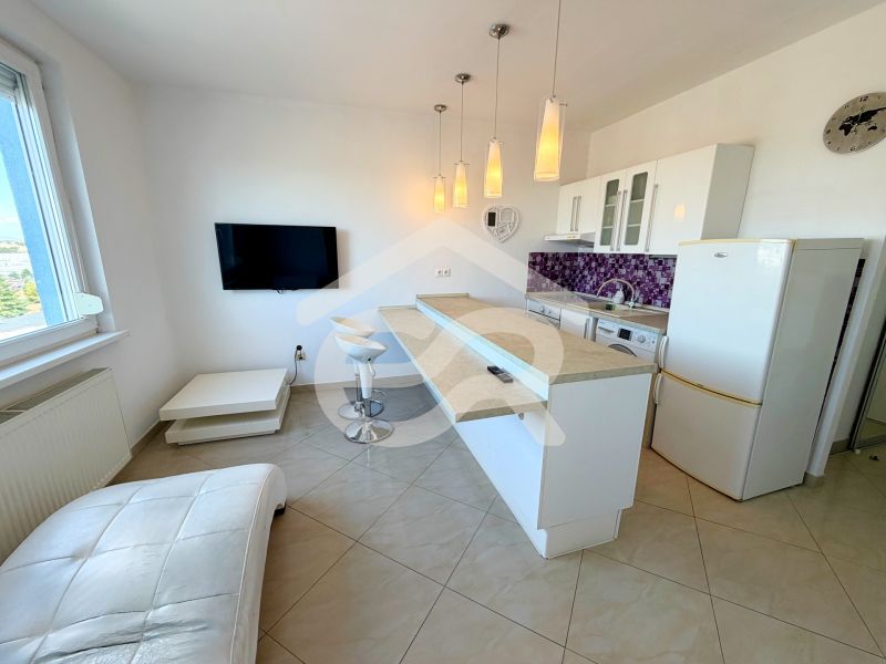 A kitchen in a studio apartment with bar stools and purple wall tiles.