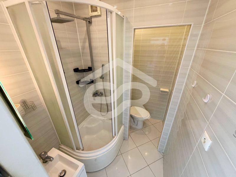 Bathroom with shower and toilet in a studio apartment, light tiles.