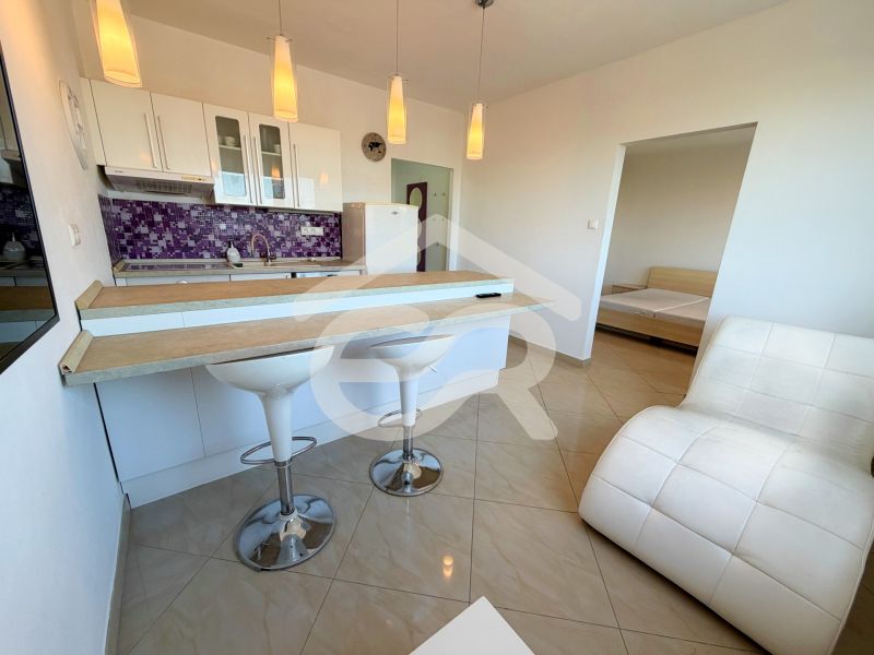 A kitchen with a bar counter in a studio apartment, white furniture, purple tiles, and an armchair.
