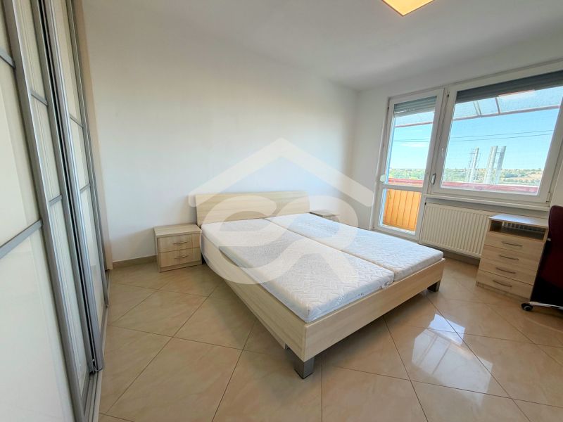 Bright bedroom in a one-room apartment with a bed, wardrobe, and balcony.