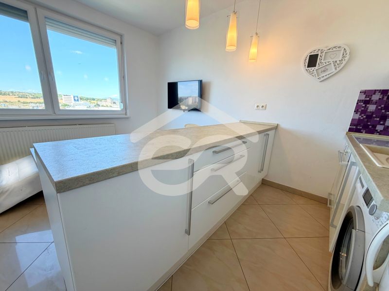 A kitchen in a studio apartment with a washing machine, white cabinets, and a countertop.