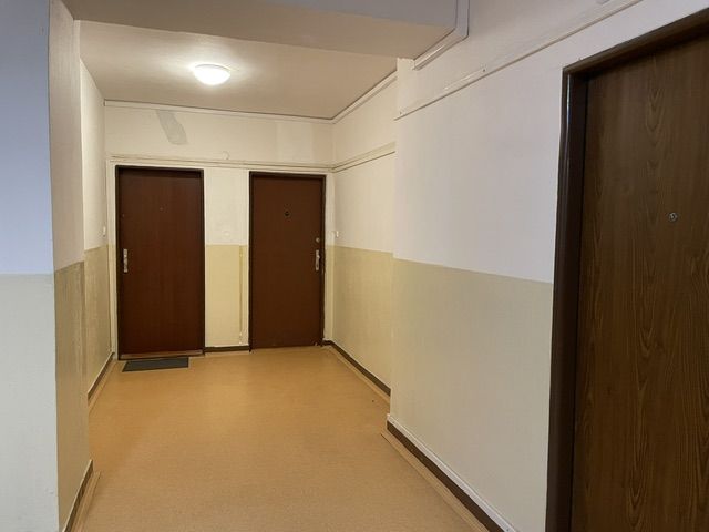 A hallway of an apartment building with three doors and a light-colored wall.