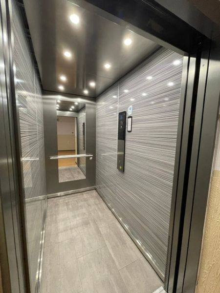 Elevator in a building with a wooden decor floor and a large mirror.