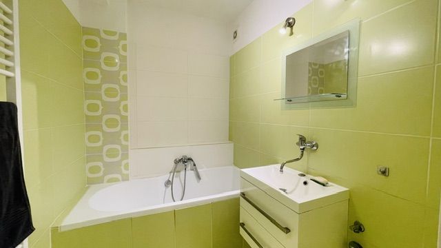 Green and white bathroom with a bathtub and a sink in a 3-room apartment.