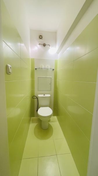 A narrow bathroom with light green tiles and a toilet in a 3-room apartment.