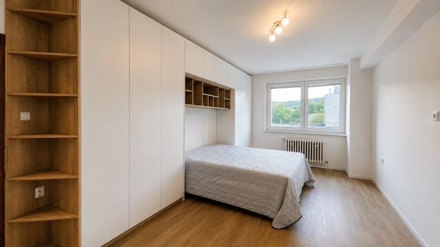 A bedroom in a three-room apartment with a bed, built-in wardrobes, and flooring with a wood decor.