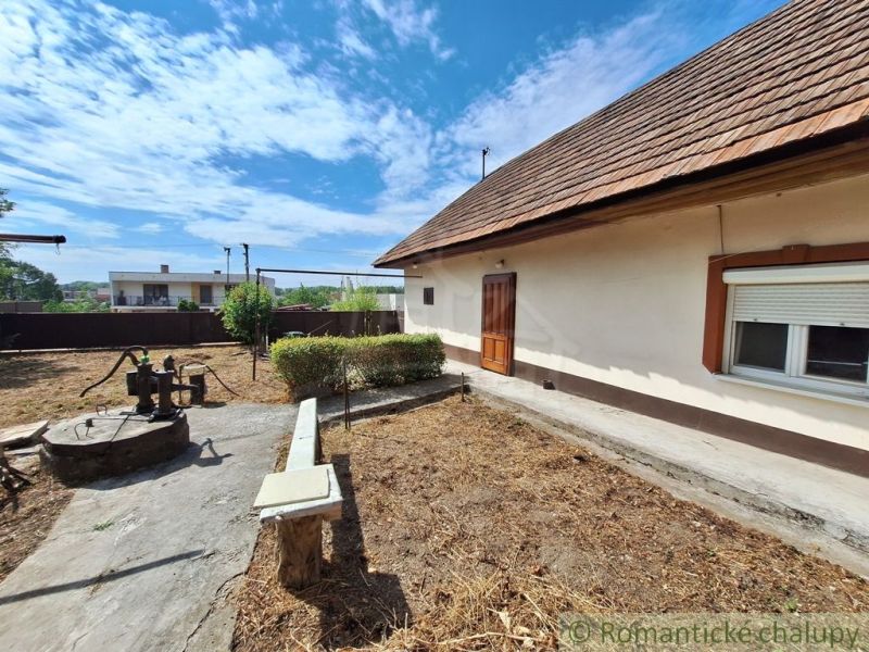 A family house in Kamenica nad Hronom with a yard, a well, and a bench on a sunny plot.