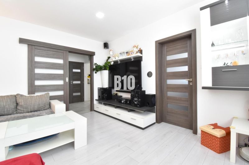 Living room in a three-room apartment with a wooden decor floor and white furniture.