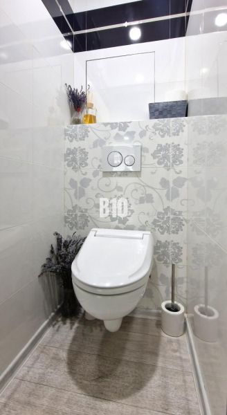 Simply furnished toilet with decorative tiles and a wooden-patterned floor.
