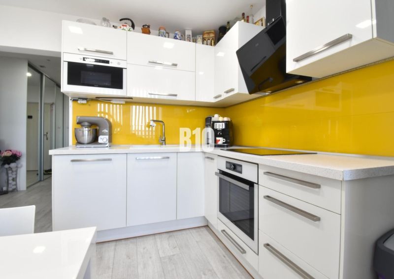 A kitchen in a 3-room apartment with white cabinets and yellow tiles.