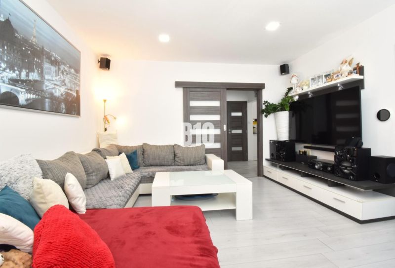 Living room in a three-room apartment with a corner sofa, television, and wooden decor flooring.