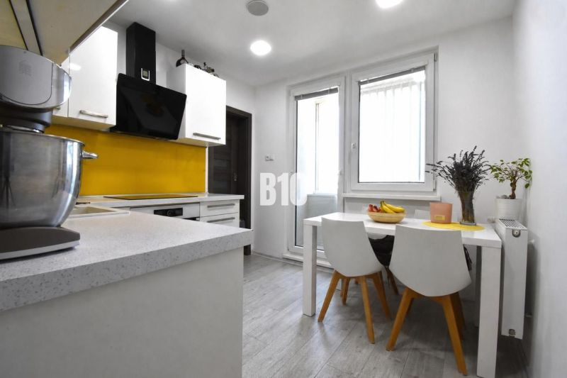 A kitchen in a 3-room apartment with white furniture and yellow tiles by the stove.