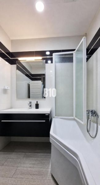 A bathroom in a 3-room apartment with a bathtub, a sink, and a floor with a wooden decor.