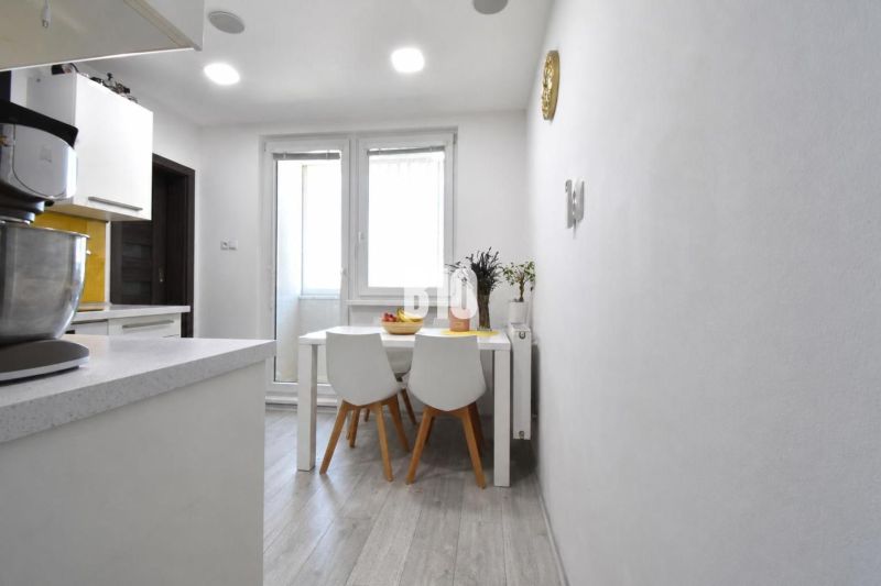 Dining area with a table and chairs on a floor with a wooden decor in a 3-room apartment.